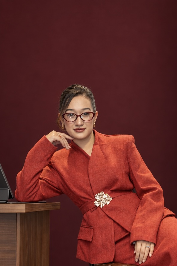 Shrija Shrestha in a rust-red suit, seated beside a desk